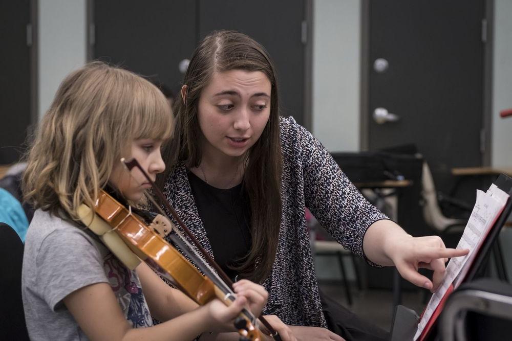 一名亿德体育音乐学生在小提琴课上与一名小学生一起工作.